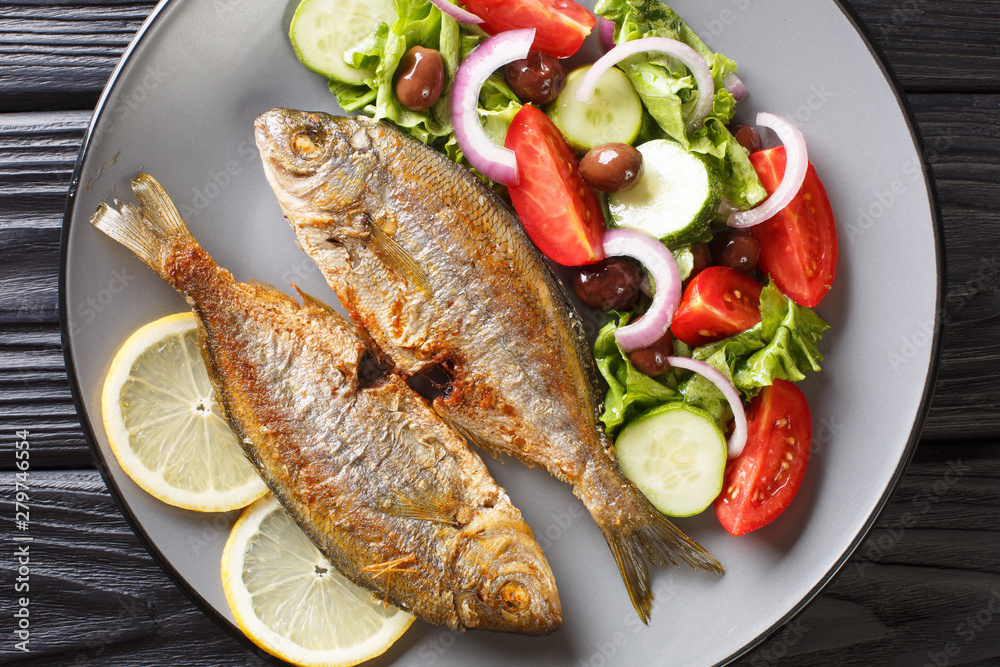 Delicious fried salpa fish with fresh vegetable salad close-up on a plate.  horizontal top view