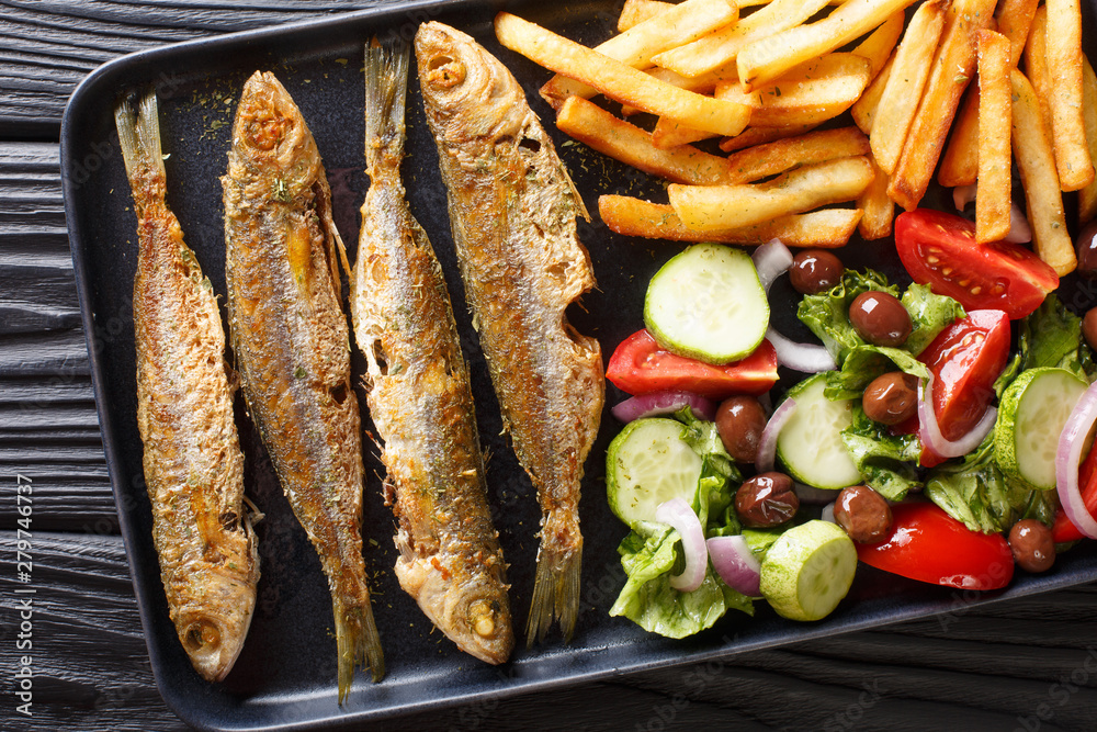 Fried boops boops fish with fresh vegetable salad and french fries close-up on a plate. horizontal top view