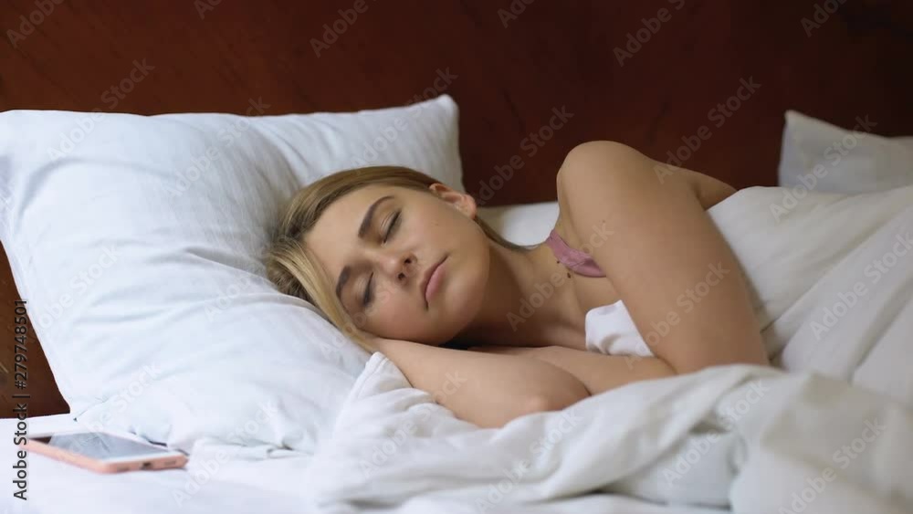 Female sleeping in bed, looking at cellphone, dont want to wake up morning alarm Female sleeping in bed, looking at cellphone, dont want to wake up morning alarm