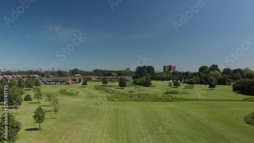 Flying over a field and trees in an urban green space on a Summer day in Manchester, England.