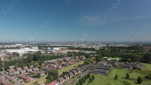 A descending shot looking out over trees and grass in an urban green space on a Summer day. Manchester, England with Manchester skyline in the background.