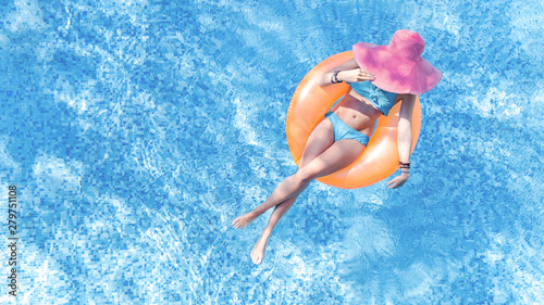 Beautiful young woman in hat in swimming pool aerial top view from above, young girl in bikini relaxes and swims on inflatable ring donut and has fun in water on family vacation, tropical holiday reso