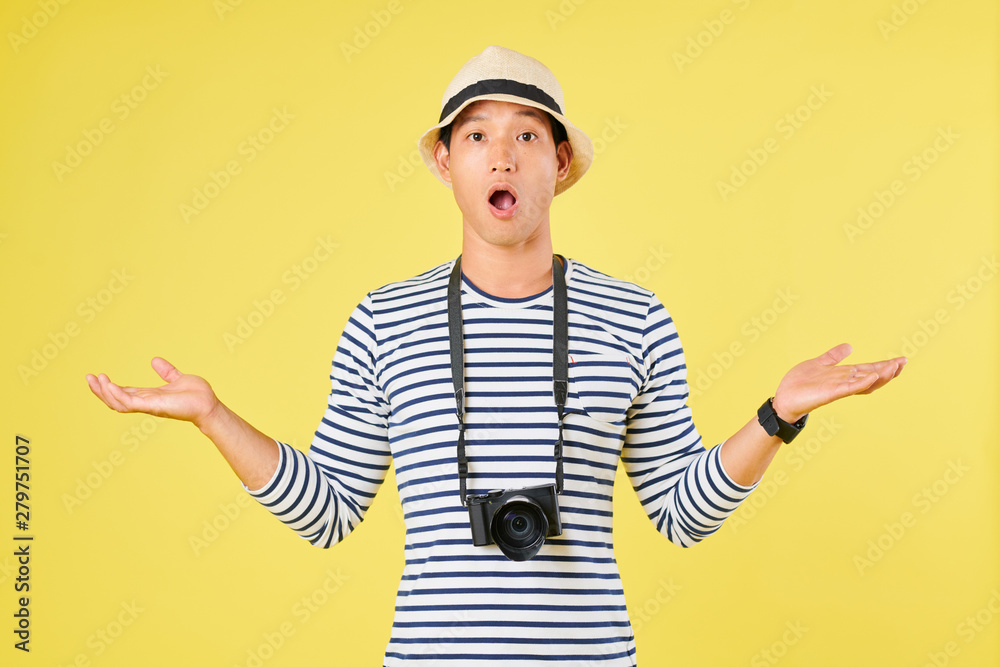 Shocked tourist with digital camera making helpless gesture, opening mouth and looking at camera