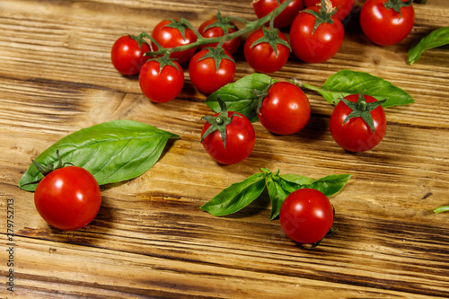 Fresh cherry tomatoes with green basil leaves on a wooden table