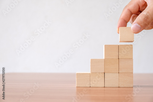 Business concept of ladder career path and growth success process. Hands of men arranging wood cube block stacking for top staircase shape on wooden table.