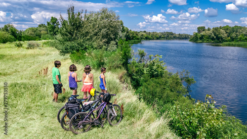 Family on bikes cycling outdoors, active parents and kids on bicycles, aerial top view of happy family with children relaxing near beautiful river from above, weekend and vacation sport and fitness co