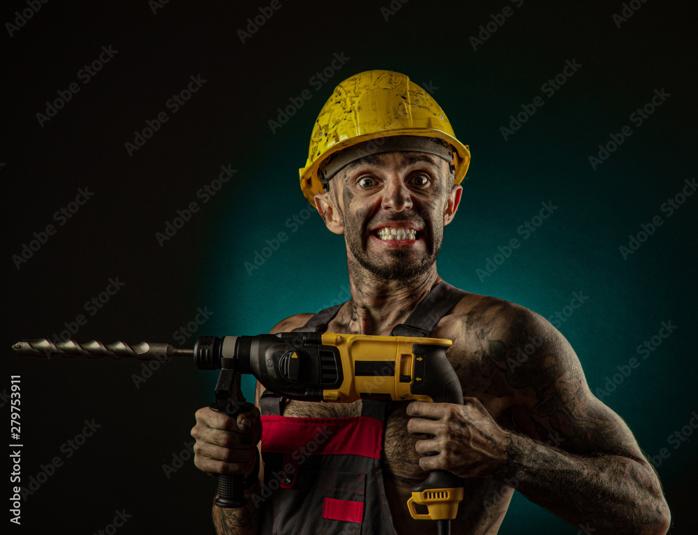 A man miner in a worker s clothes and a helmet, dirty, in soot, with a naked body, grimaces at the camera