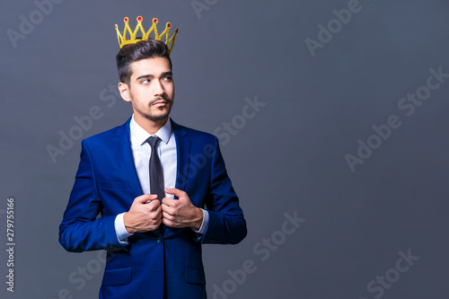 A young man with a crown on his head on a gray background looks to the side