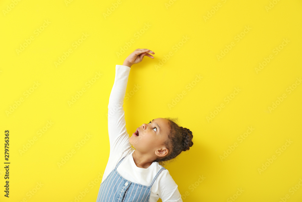 Cute little African-American girl measuring height near color wall - obrazy, fototapety, plakaty 