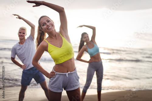 Group of people doing exercises on the beach. Fitness, training, sport and people concept
