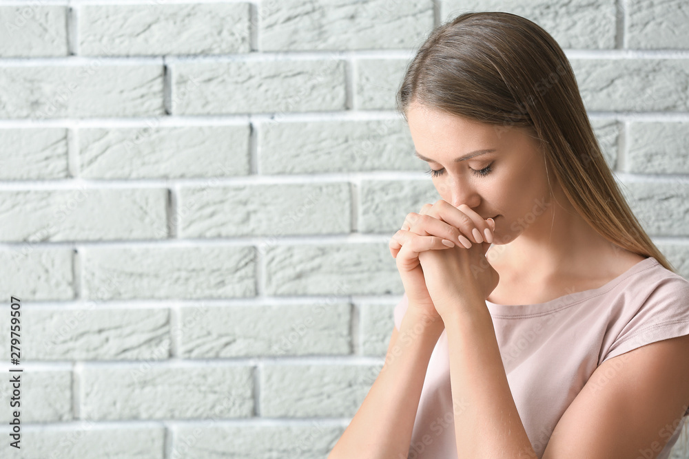 Religious young woman praying against brick wall Religious young woman praying against brick wall