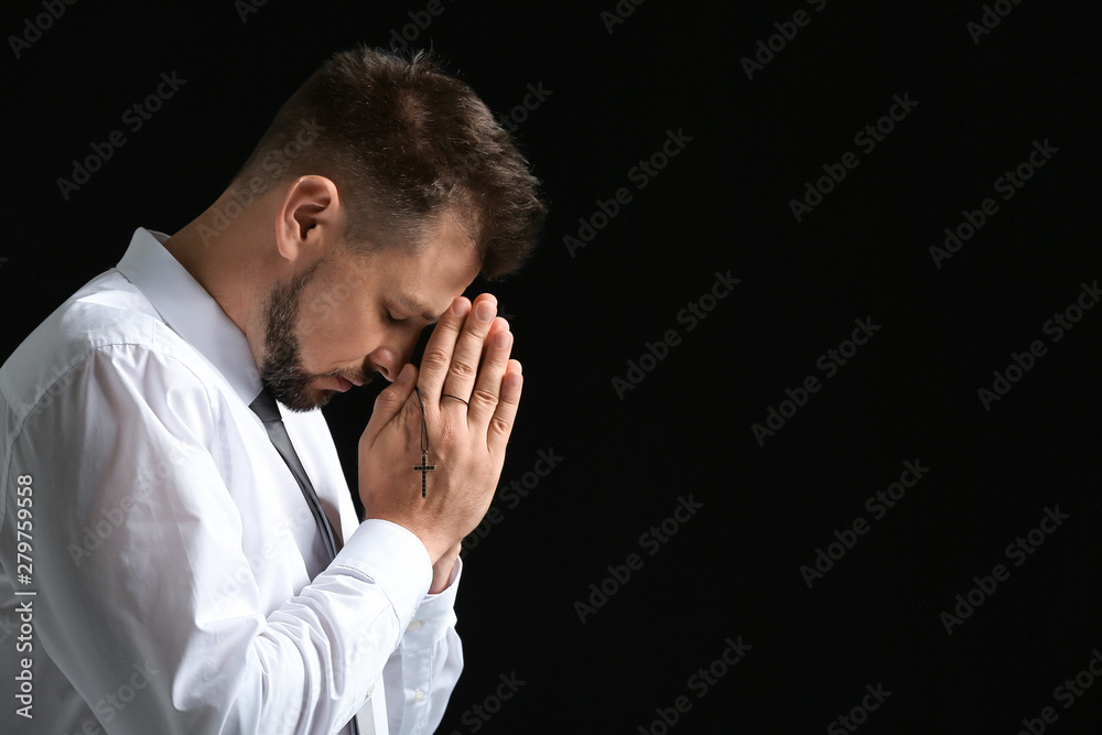 Religious man praying on dark background Religious man praying on dark background