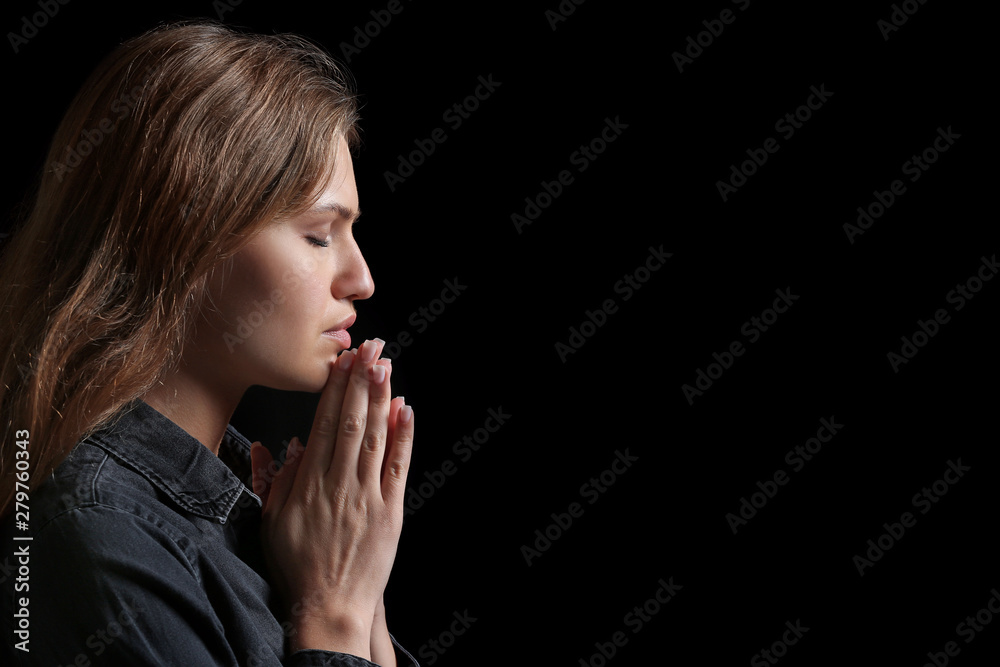 Religious young woman praying to God on dark background Religious young woman praying to God on dark background