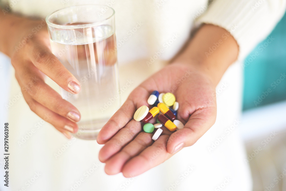 Take a medicine health care and people concept - Many multi colors pills in hand woman and taking with water glass Take a medicine health care and people concept - Many multi colors pills in hand woman and taking with water glass