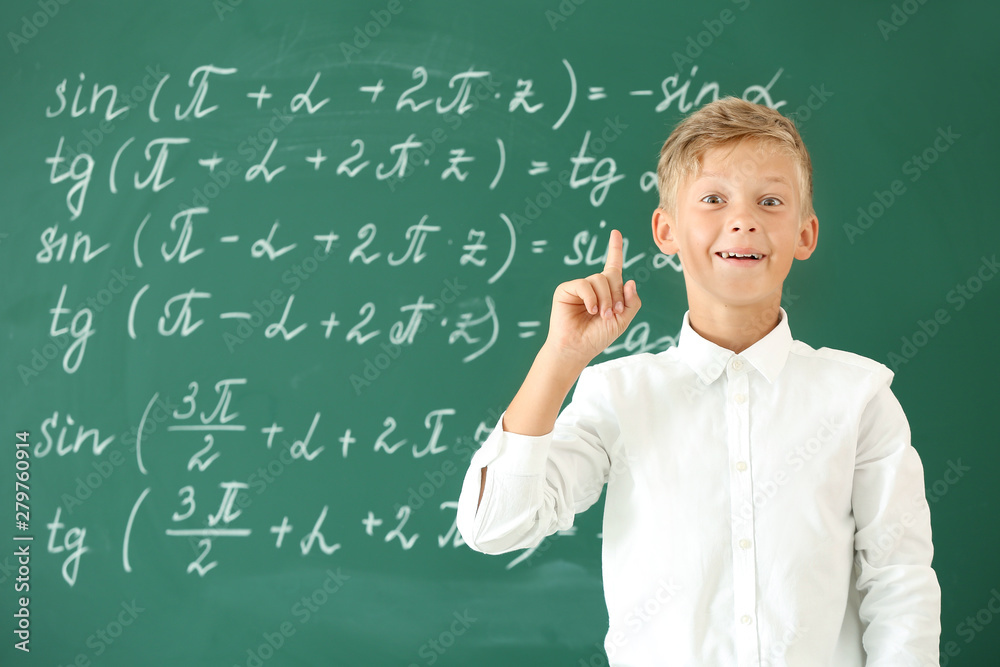 Little boy with raised index finger near school blackboard in classroom Little boy with raised index finger near school blackboard in classroom