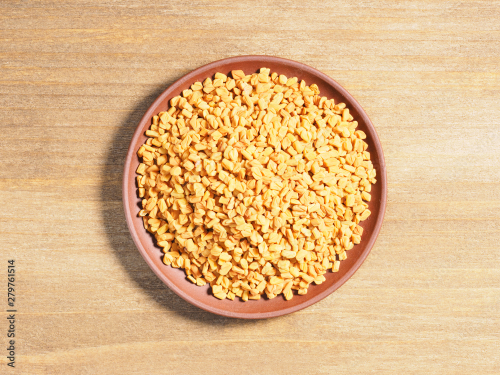 Spice Fenugreek (Trigonetla) on a brown clay plate on a wooden background