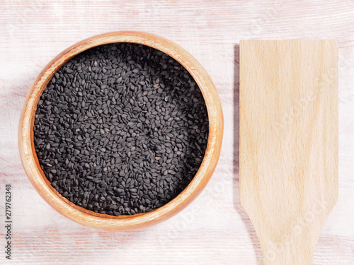 Black sesame (Sesamum) in brown wooden cup on wooden background with spoon