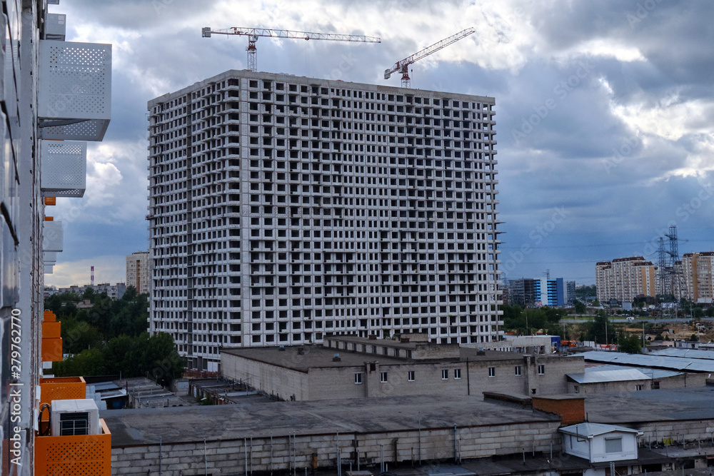 Building a house against a stormy sky. Multi-storey building and tower cranes in the process of construction.