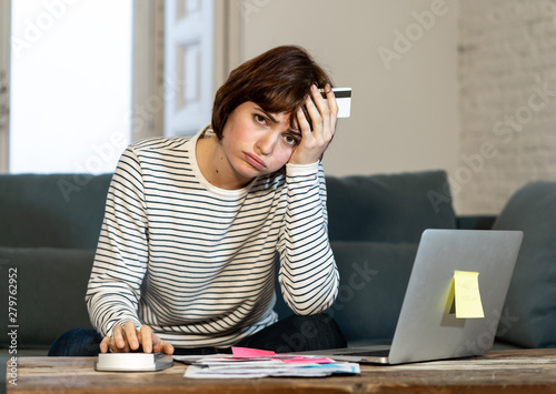 Stressed and overwhelmed young woman paying credit card debts and bills on laptop