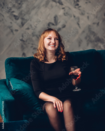 Attractive happy woman in little black dress and heels, with the red lips, fault holding a glass of wine.