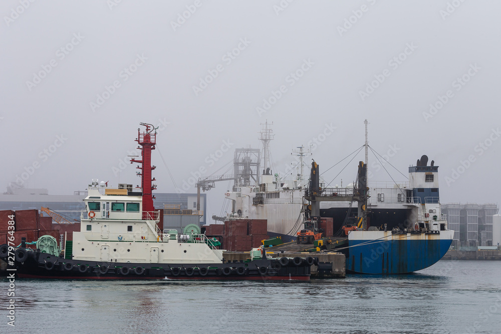 a tugboat docking at a dock and a cargo ship carrying cargo.