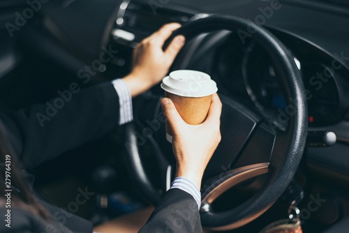 Business woman's hand holding a coffee cup to take away, she is driving in the morning