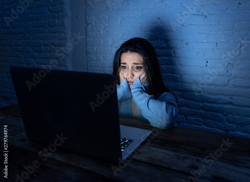 Foto Scared woman on laptop in the dark feeling fear suffering online harassment and
