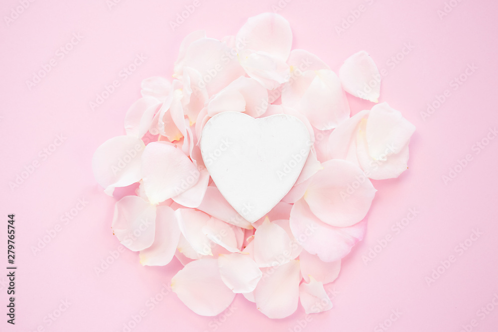 Decorative white heart with flower petals on a pink background. Flat lay.