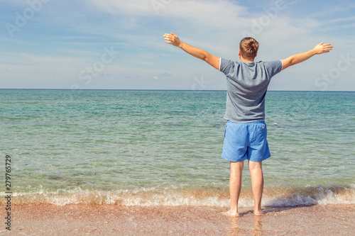 Young man in a t-shirt on the seashore and looks at the sea, back view