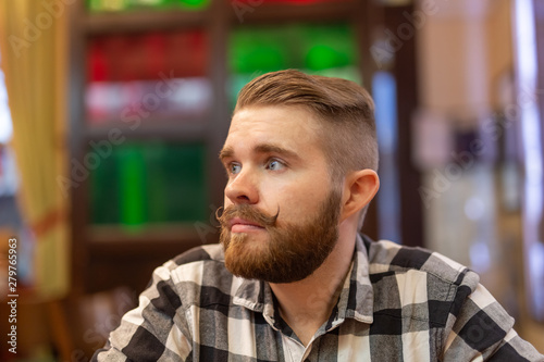 Portrait of a handsome thoughtful young man with a mustache and beard looking away in a cafe on a blurred background. The concept of student or stylish men.