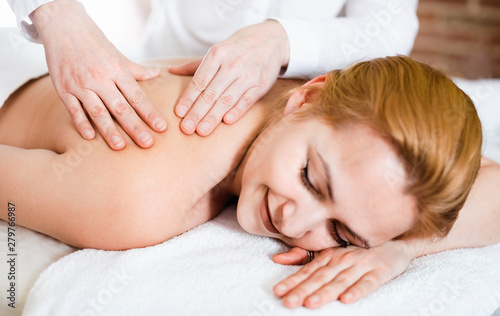 Adult masseuse makes relaxing massage shoulder zone to young woman