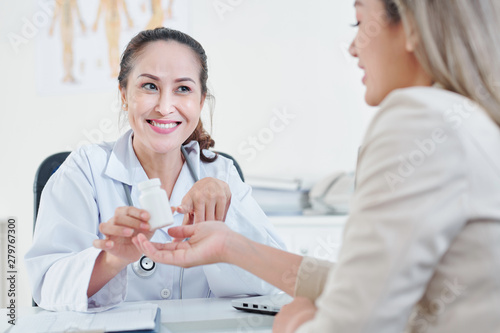 Smiling mature Vietnamese female physician explaining young woman how to take vitamins and supplements