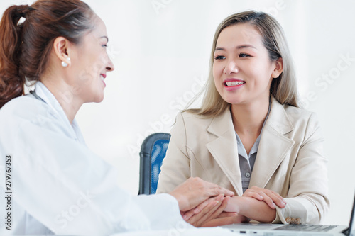 Cheerful mature Vietnamese doctor congratulating young female patient with recovery