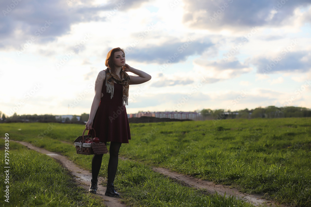A girl in a hat on a walk in the park. A girl with a basket walks in the spring. A girl is walking along the road at sunset.