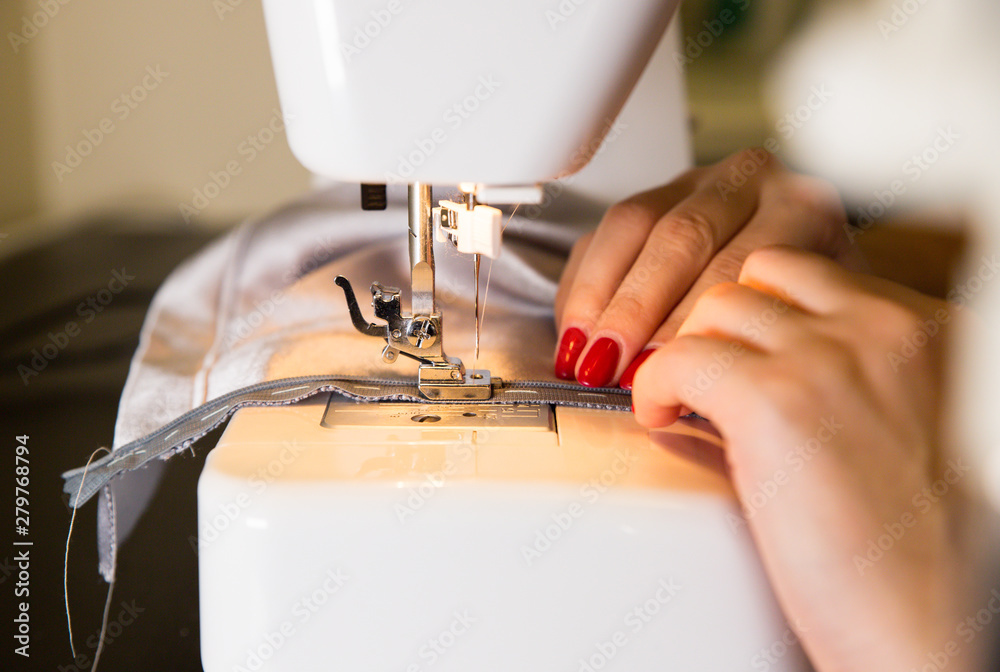 Woman is working at sewing machine. Girls hands with red manicure. Fashion concept. Creating of new clothes process. Hobby ideas.