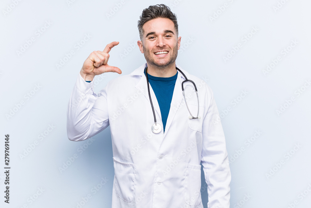 Young handsome doctor man holding something little with forefingers, smiling and confident. Young handsome doctor man holding something little with forefingers, smiling and confident.