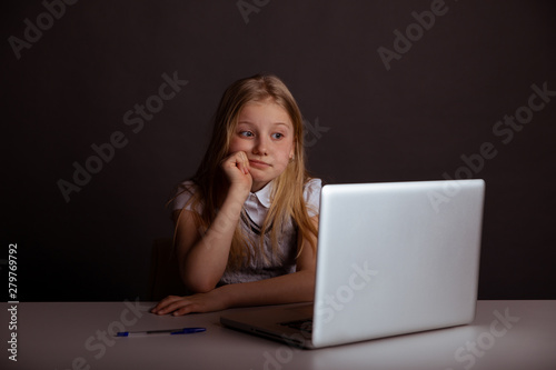 Bored little girl sitting on at the table and using computer isolated