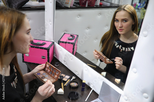 A young girl does make-up in a beauty salon. The girl in front of the mirror is making up. Beauty saloon.