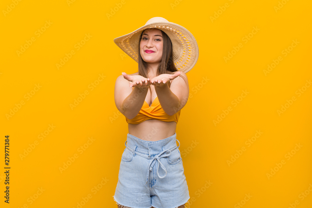 Young caucasian woman wearing a straw hat, summer look holding something with palms, offering to camera. Young caucasian woman wearing a straw hat, summer look holding something with palms, offering to camera.
