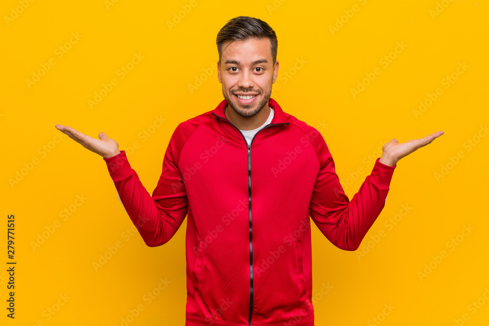 Young filipino fitness man makes scale with arms, feels happy and confident. Young filipino fitness man makes scale with arms, feels happy and confident.