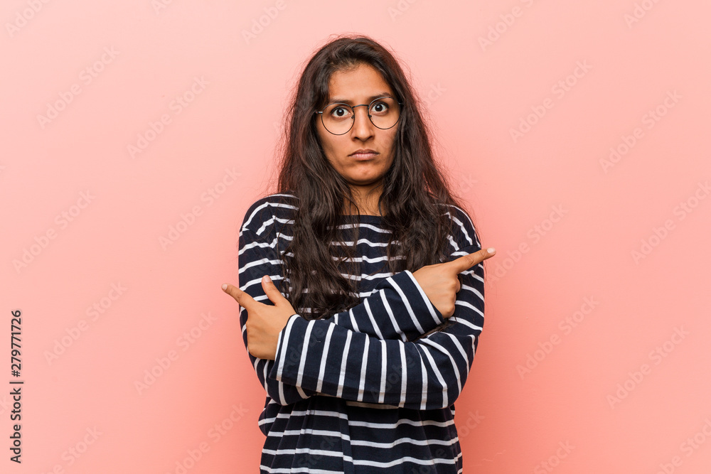 Young intellectual indian woman points sideways, is trying to choose between two options. Young intellectual indian woman points sideways, is trying to choose between two options.