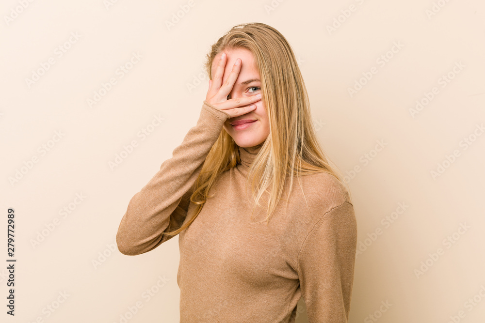 Cute and natural teenager woman blink at the camera through fingers, embarrassed covering face.