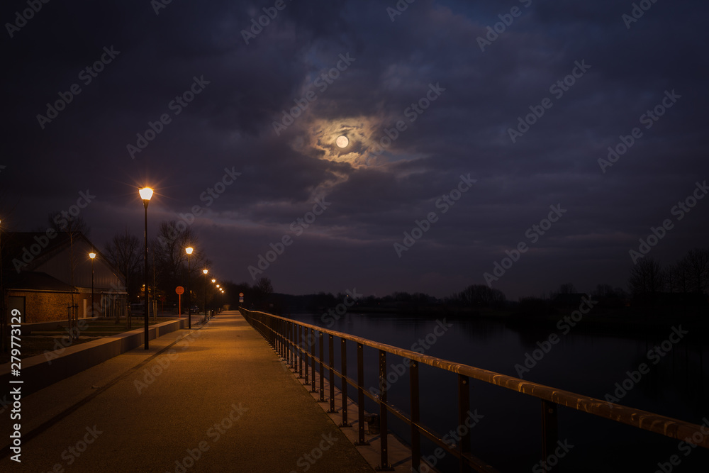 Fototapeta premium the full moon comes squeaking among the dramatic clouds on the Leie in Wervik, Belgium