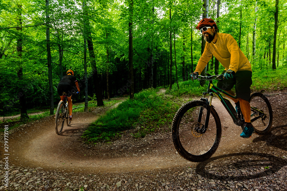 Obraz premium Cycling woman and men riding on bikes at sunset mountains forest landscape. Couple cycling MTB enduro flow trail track. Outdoor sport activity.