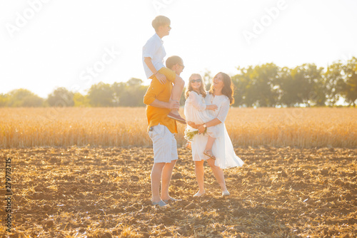 Photo of a happy family having time in a field of wheat, on golden sun light