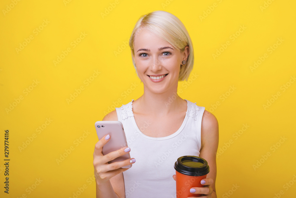 Take a break ! Photo of a blond woman, using mobile and drink some coffee, on a break, standing over yellow background Take a break ! Photo of a blond woman, using mobile and drink some coffee, on a break, standing over yellow background