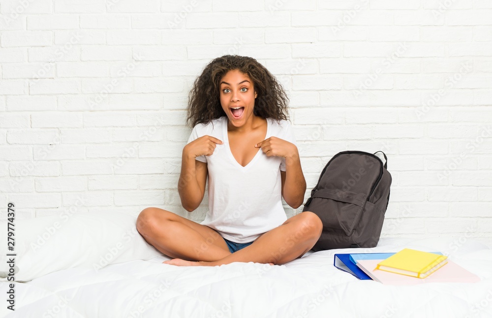 Young african american student woman on the bed surprised pointing with finger, smiling broadly. Young african american student woman on the bed surprised pointing with finger, smiling broadly.