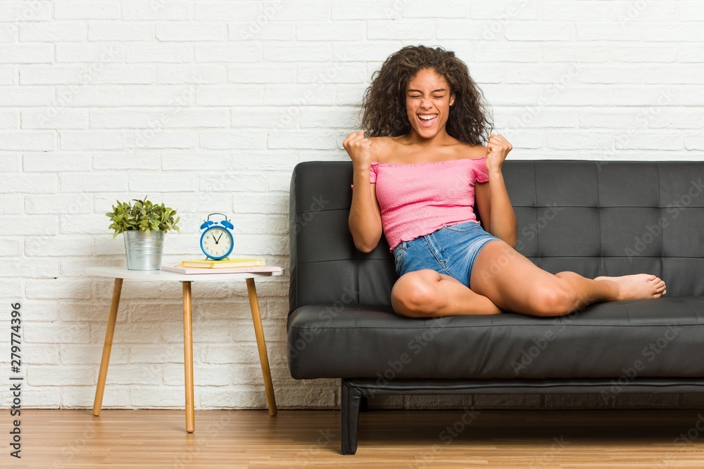Young african american woman sitting on the sofa cheering carefree and excited. Victory concept. Young african american woman sitting on the sofa cheering carefree and excited. Victory concept.