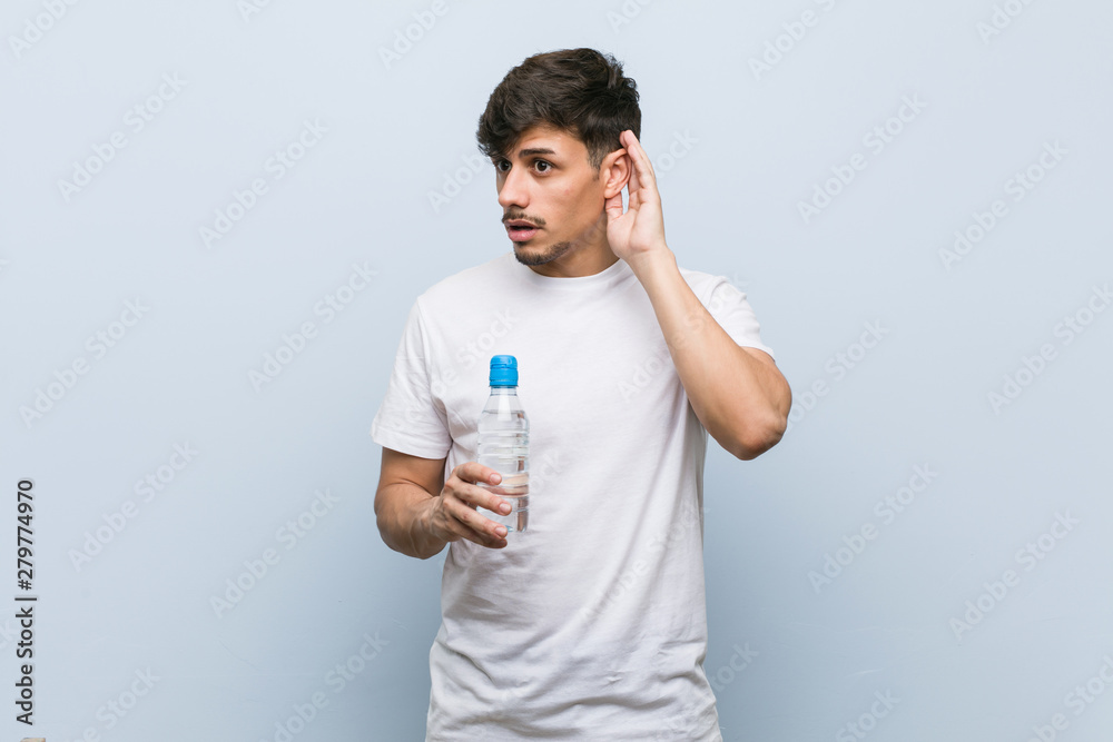 Young hispanic man holding a water bottle trying to listening a gossip. Young hispanic man holding a water bottle trying to listening a gossip.
