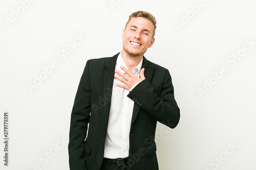 Young caucasian business man laughs out loudly keeping hand on chest.